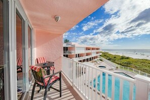 A balcony with a pool, a table with chairs, and a view of the beach and ocean. - Amic 42 2 Bedroom Condo (Bradenton Beach)