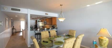Een eethoek met een glazen tafel en stoelen, een keuken op de achtergrond en een lamp op een bijzettafeltje.