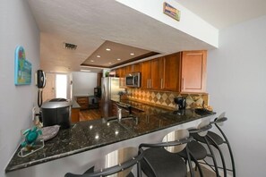 A kitchen with a central island, wooden cabinets, and a microwave. - Amic 42 2 Bedroom Condo (Bradenton Beach)