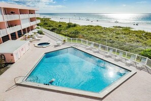 Une piscine avec vue sur la plage et l’océan, entourée d’une clôture blanche et bordée d’un immeuble doté de balcons.