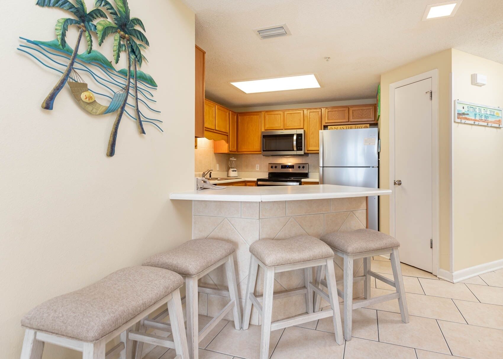 A kitchen with wooden cabinets, a microwave, a refrigerator, and a bar stool seating area.