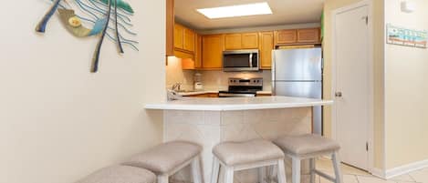A kitchen with wooden cabinets, a microwave, a refrigerator, and a bar stool seating area.
