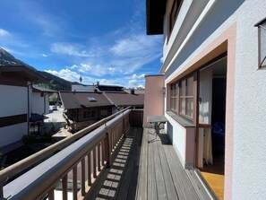 Eine Holzdachterrasse mit Geländer, einem Tisch und einer Bank, mit Blick auf eine gebirgige Landschaft.