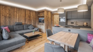 A modern living room with a grey sectional sofa, a wooden coffee table, and a dining area with a wooden table and chairs. - Premium Apartment in the City Center (Kirchberg in Tirol)