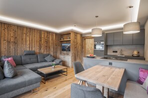 Ein modernes Wohnzimmer mit einem grauen Ecksofa, einem Holztisch und einem Essbereich mit Holztisch und Stühlen.