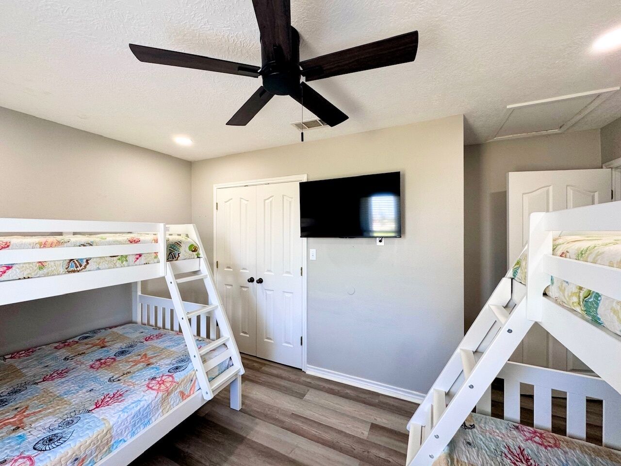 A room with bunk beds, a ceiling fan, a television, and a door.