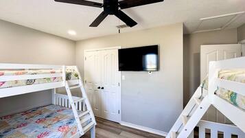 A room with bunk beds, a ceiling fan, a television, and a door.