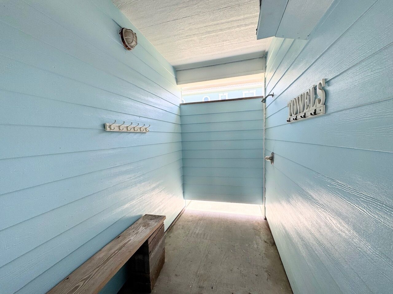 A narrow hallway with a bench, a towel rack, and a door at the end.