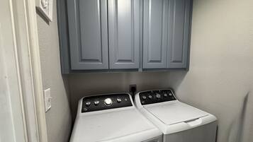 A laundry room with two stacked washers and dryers, grey cabinets above, and a white wall.