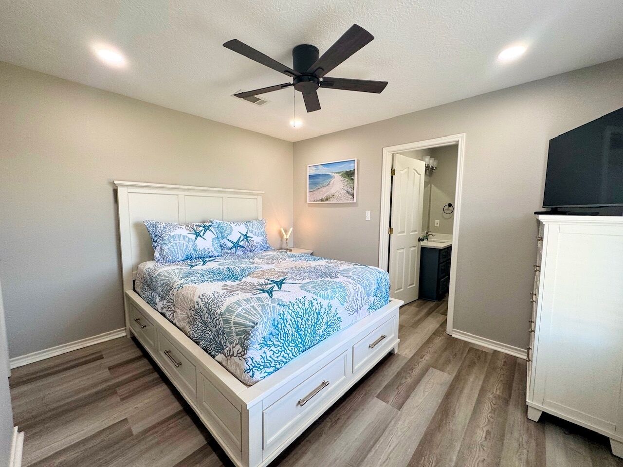 A bedroom with a bed, a ceiling fan, a nightstand, a door, and a cabinet.