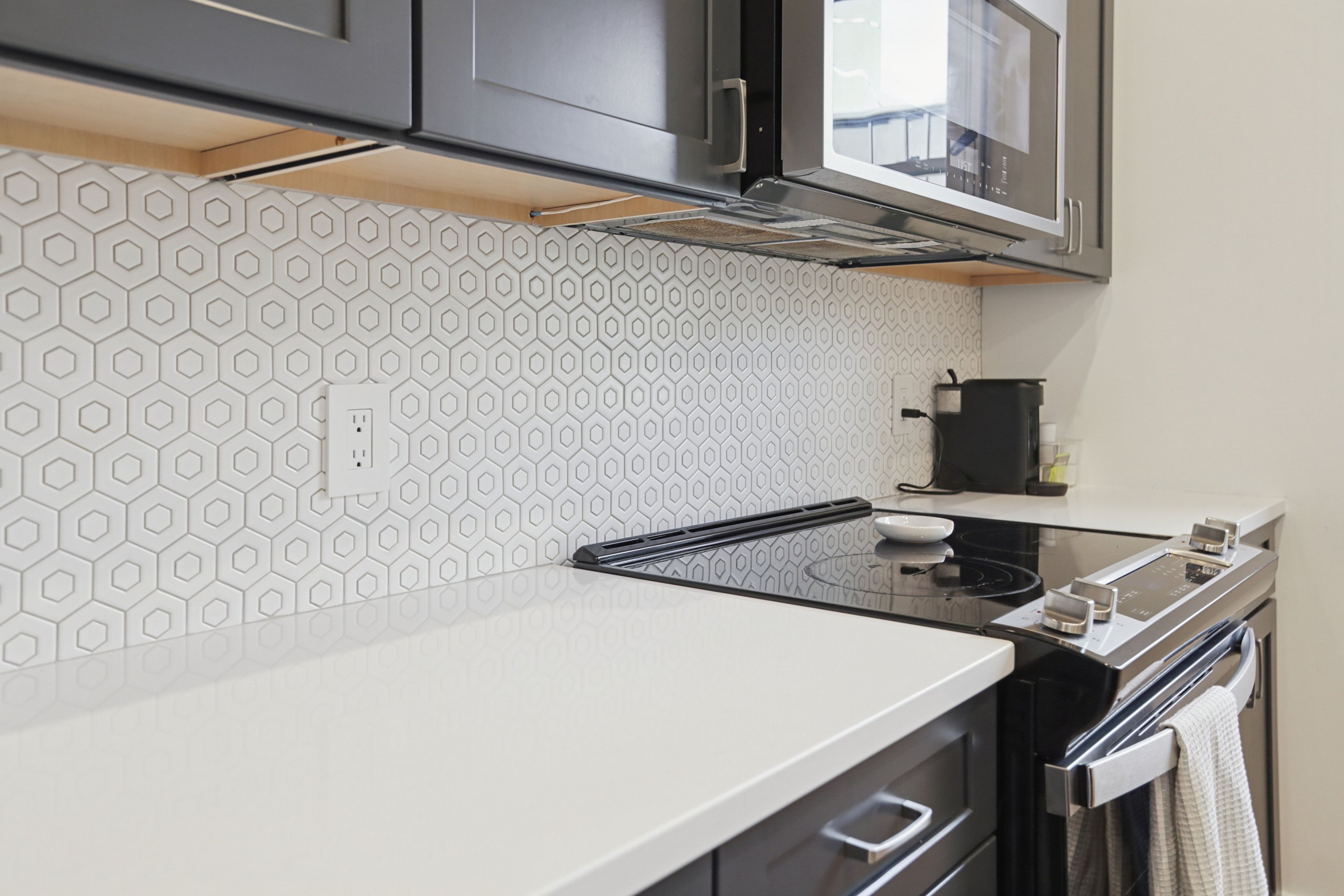 Een moderne keuken met een backsplash met een hexagonaal patroon, roestvrijstalen apparatuur en een wit aanrecht.