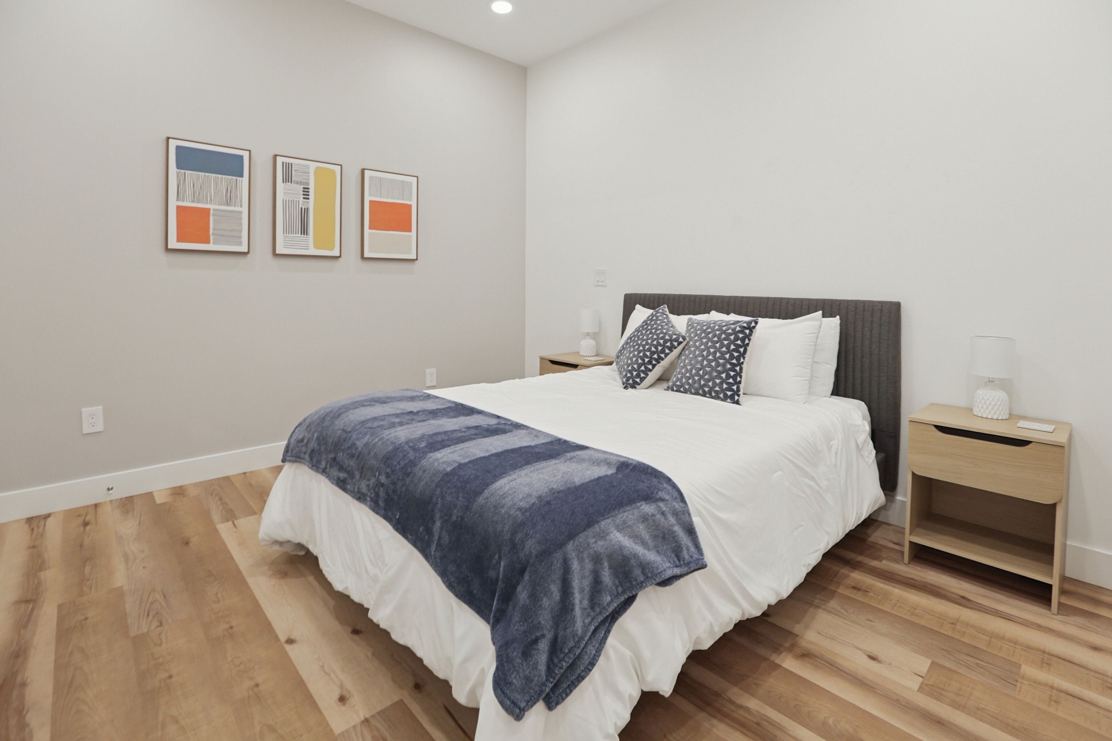 A modern bedroom with a large bed, a bedside table, and a nightstand. There are three framed artworks on the wall.