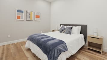 A modern bedroom with a large bed, a bedside table, and a nightstand. There are three framed artworks on the wall.