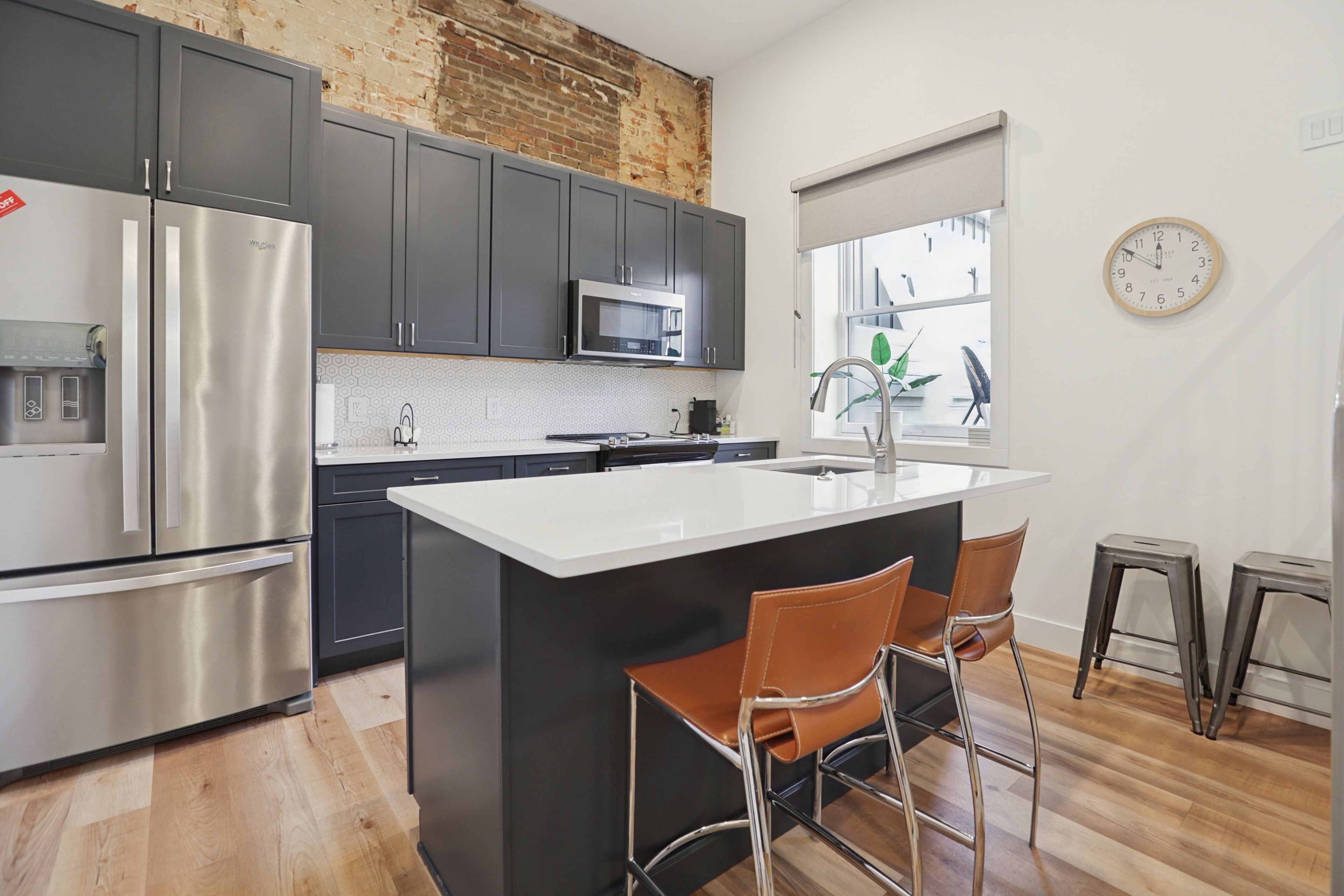 A modern kitchen with stainless steel appliances, a central island with bar stools, and a brick wall.