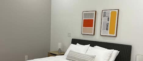 Un dormitorio moderno con cama, mesitas de noche y una obra de arte en la pared.