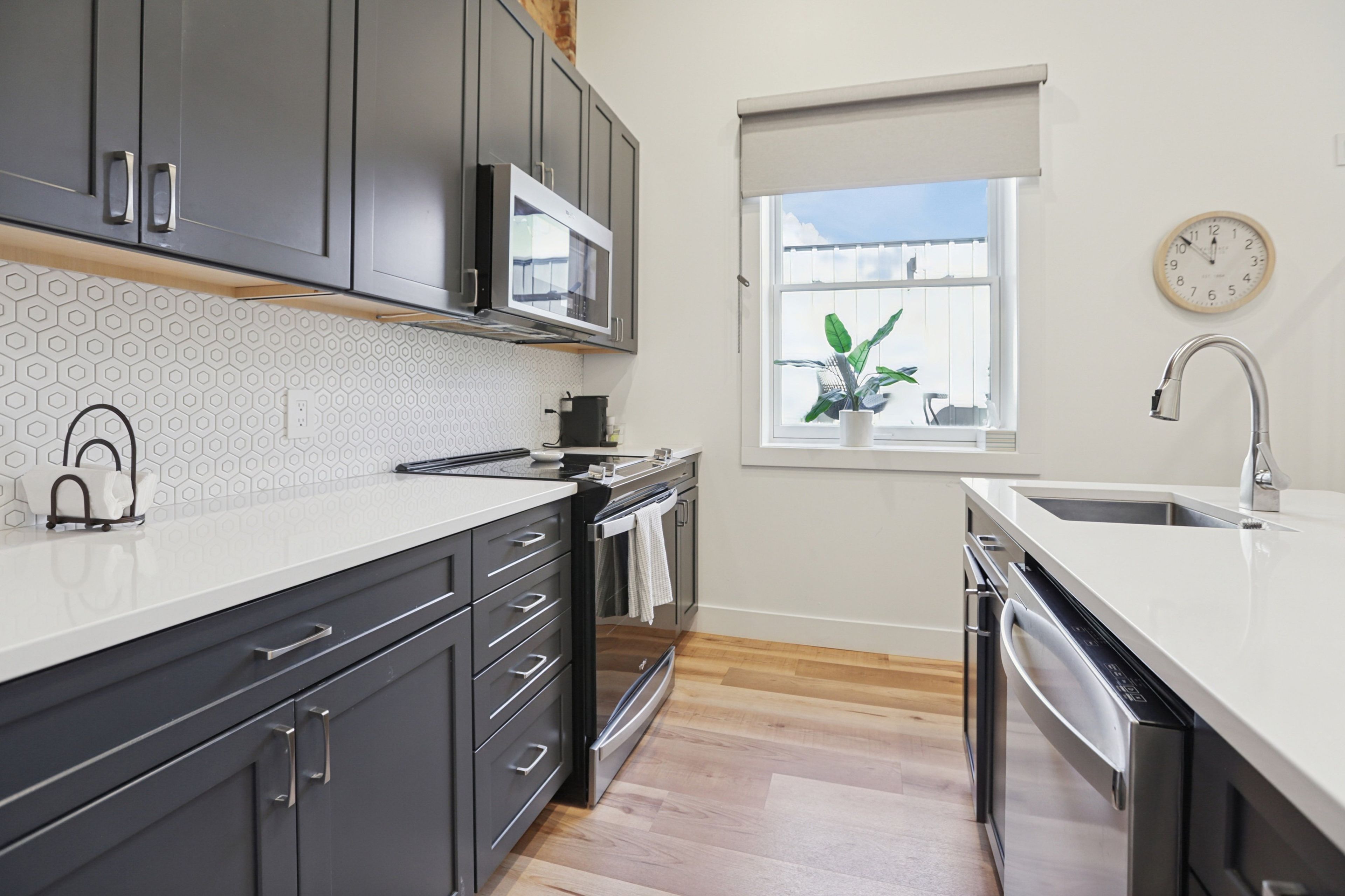 A modern kitchen with dark cabinets, a microwave, a sink, and a window with a plant.