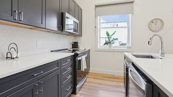 A modern kitchen with dark cabinets, a microwave, a sink, and a window with a plant.