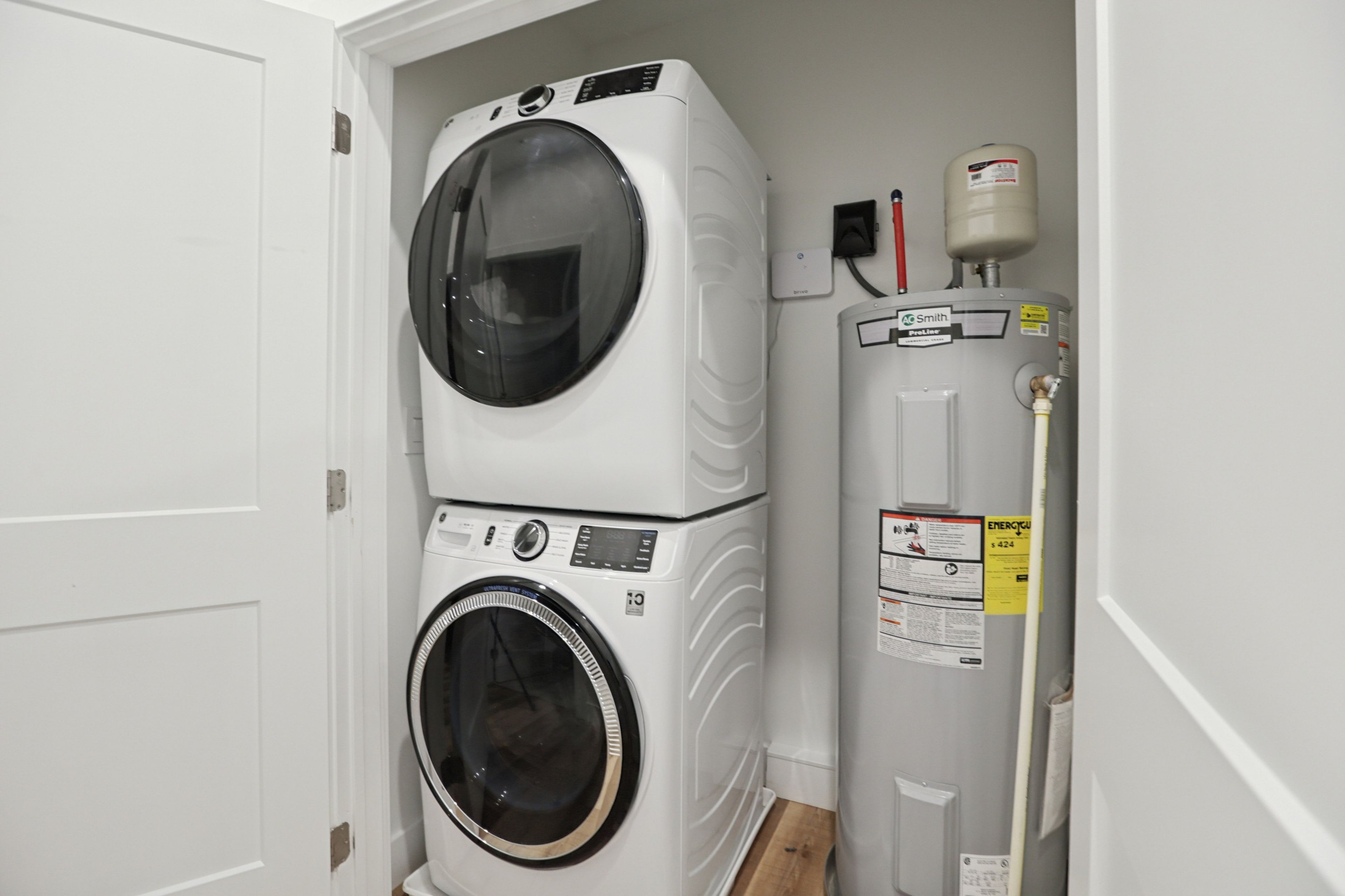 A laundry room with stacked washers and dryers, a water heater, and a pipe.
