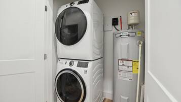A laundry room with stacked washers and dryers, a water heater, and a pipe.
