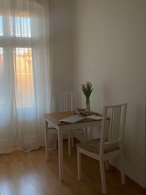 A room with a wooden table, two white chairs, a vase with flowers, and a window with sheer curtains. - Copy of To complete (Görlitz)