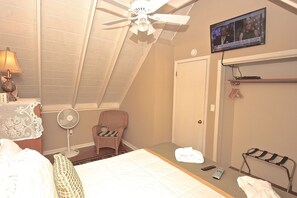 Une chambre à coucher avec un lit, une chaise, un ventilateur, une télévision et un ventilateur de plafond.