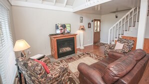 Ein Wohnzimmer mit Kamin, einer Couch, einem gemusterten Sessel, einem Fernseher und einer Treppe.