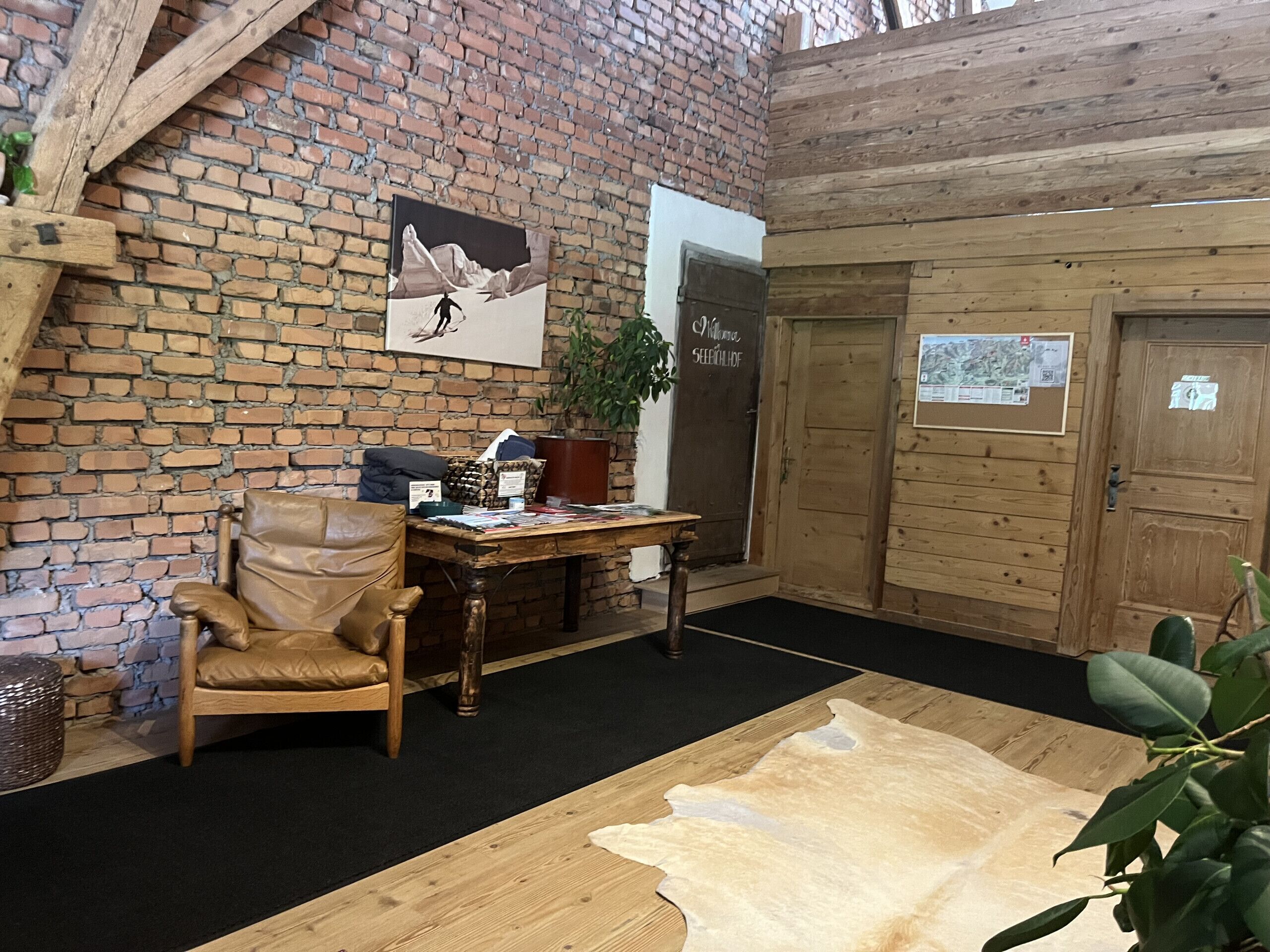 A room with a brick wall, a wooden desk, a leather chair, a wooden table, and a mounted painting.