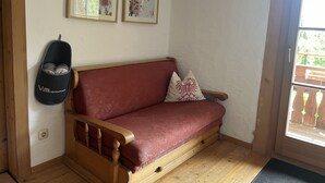 Eine hölzerne Bank mit rotem Kissen, ein an der Wand befestigter Babywippen und zwei gerahmte Blumenbilder.
