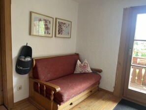 Eine hölzerne Bank mit rotem Kissen, ein an der Wand befestigter Babywippen und zwei gerahmte Blumenbilder.