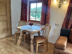 A dining area with a wooden table, two chairs, a bench, and a window with curtains. - Seebichlhof 2 - Lebenberg (Kitzbühel)