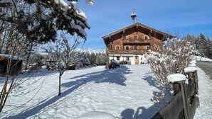 Eine Holzhütte mit Balkon, umgeben von schneebedeckten Bäumen und blauem Himmel.