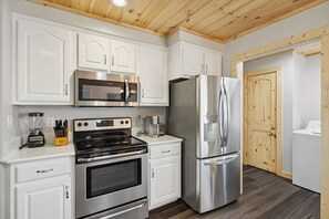 Une cuisine moderne avec des meubles blancs, des appareils en acier inoxydable et un plafond en bois.