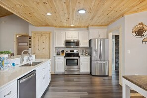 A modern kitchen with white cabinets, stainless steel appliances, and a wooden ceiling. - Majestic Valley View 3 Bedroom Cabin (Sevierville)