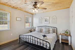 Une chambre à coucher avec un lit, un ventilateur de plafond, une table de chevet et des œuvres d’art murales.