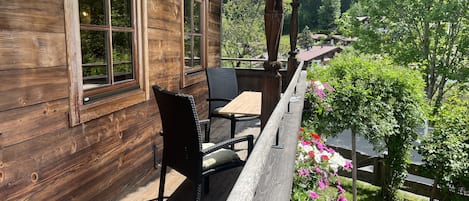 Una terraza de madera con una mesa y sillas, con vista a un jardín con flores y una valla de madera.