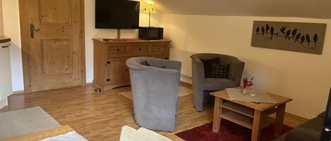 A furnished living room with a wooden cabinet, a television, a sofa, a small table, and a red rug.