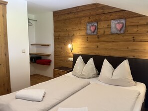 A bedroom with a wooden headboard, two beds with white linens, a bedside table, a wall-mounted light, and a closet with a hanging rack. - Seebichlhof 4 - Horn (Kitzbühel)