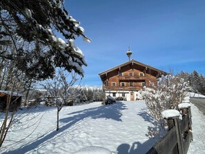 A wooden building with a sloped roof and a bell tower, surrounded by snow-covered trees and a clear sky. - Seebichlhof 4 - Horn (Kitzbühel)