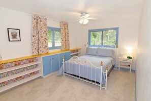 A bedroom with a bed, a nightstand, a window, a ceiling fan, and built-in storage with patterned curtains.