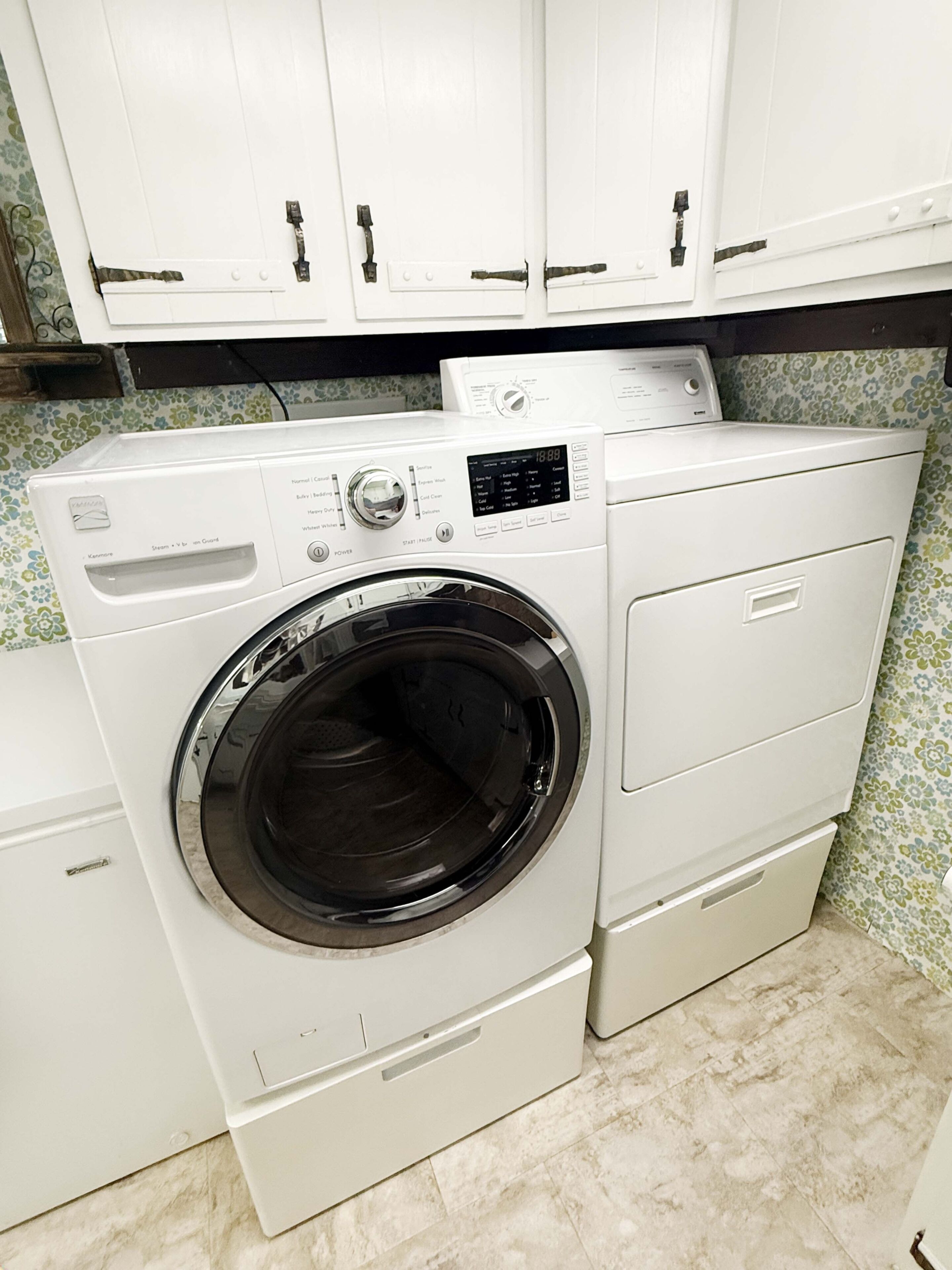 A front-loading washing machine with a control panel, a dryer, and a cabinet above.