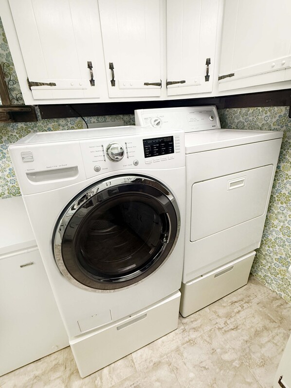 A front-loading washing machine with a control panel, a dryer, and a cabinet above.