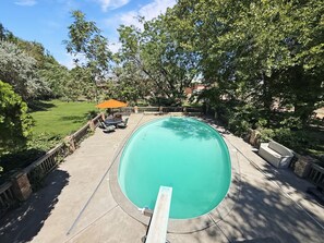A swimming pool with a surrounding deck, a patio area with outdoor furniture, and a view of a residential neighborhood.