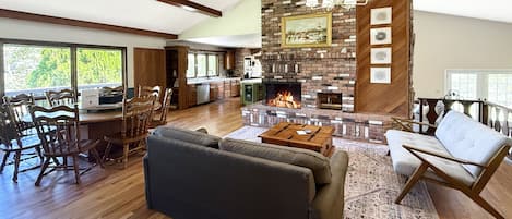 A spacious living area with a fireplace, wooden flooring, and a dining area with wooden furniture.