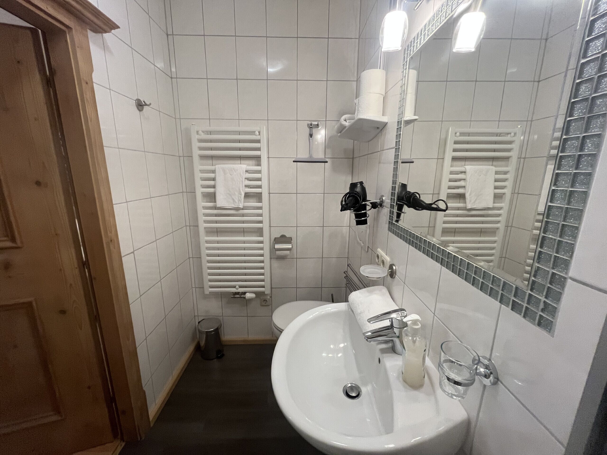 Kylpyhuone, jossa on valkoinen pesuallas, peili, pyyhekoukku ja wc-istuin.