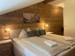 Ein ordentlich bezogenes Bett mit Kissen und einem gefalteten Handtuch, ein Wandbild und zwei Wandleuchten.