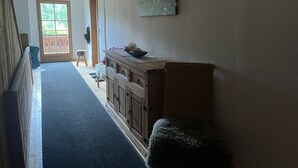 Een gang met een houten bank, een rieten stoel en een kastje met een kom erboven.