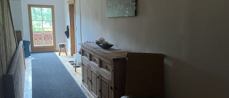 A hallway with a wooden bench, a wicker chair, and a cabinet with a bowl on top.