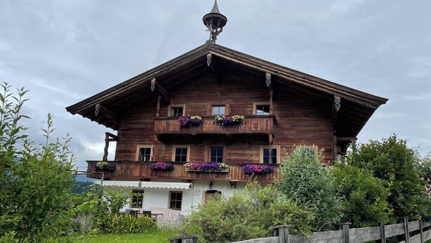 Een klassieke houten chalet met balkon, omgeven door groen.