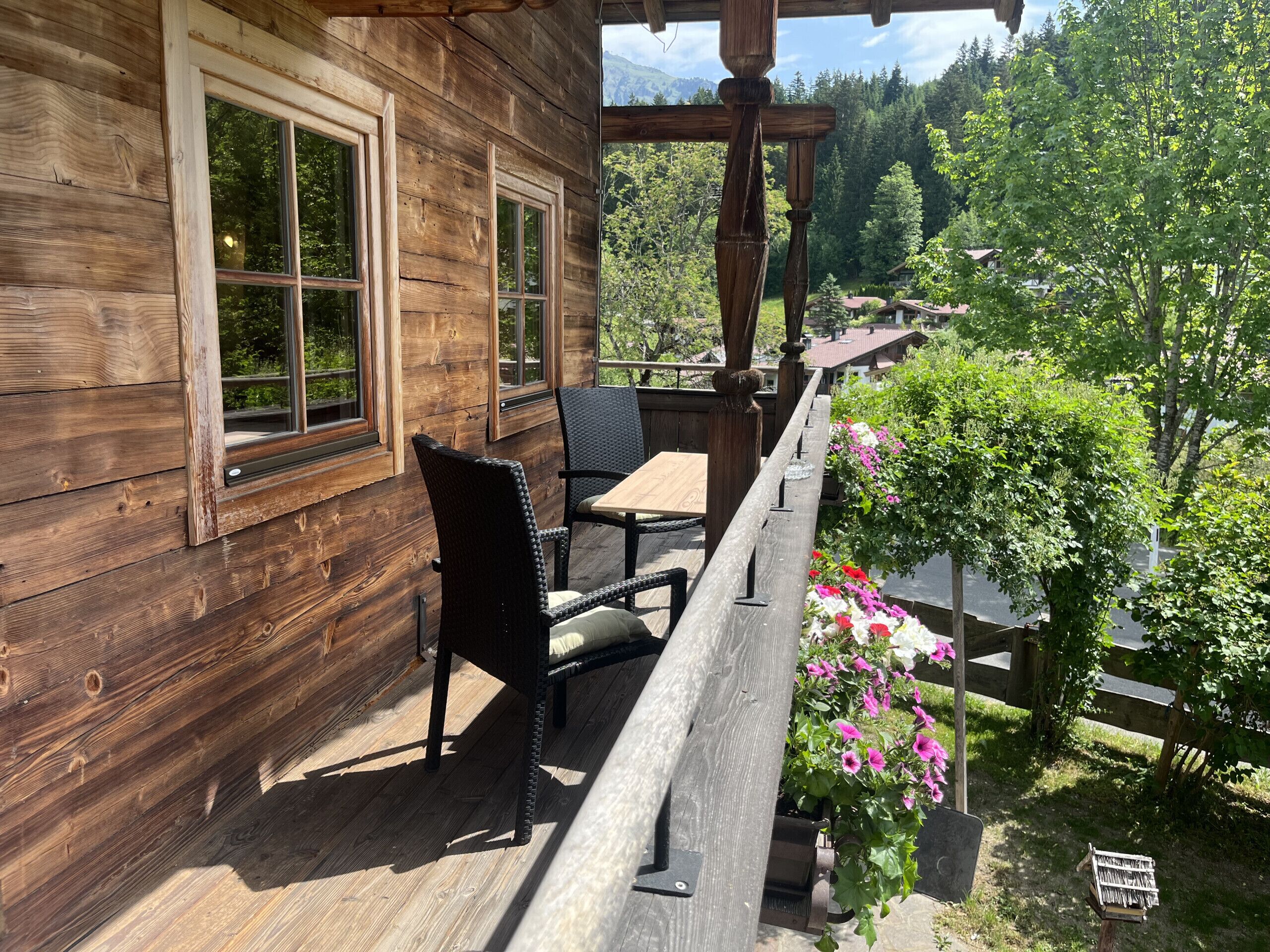 Une terrasse en bois avec une table et des chaises, donnant sur un jardin fleuri et bordé d’une clôture en bois.