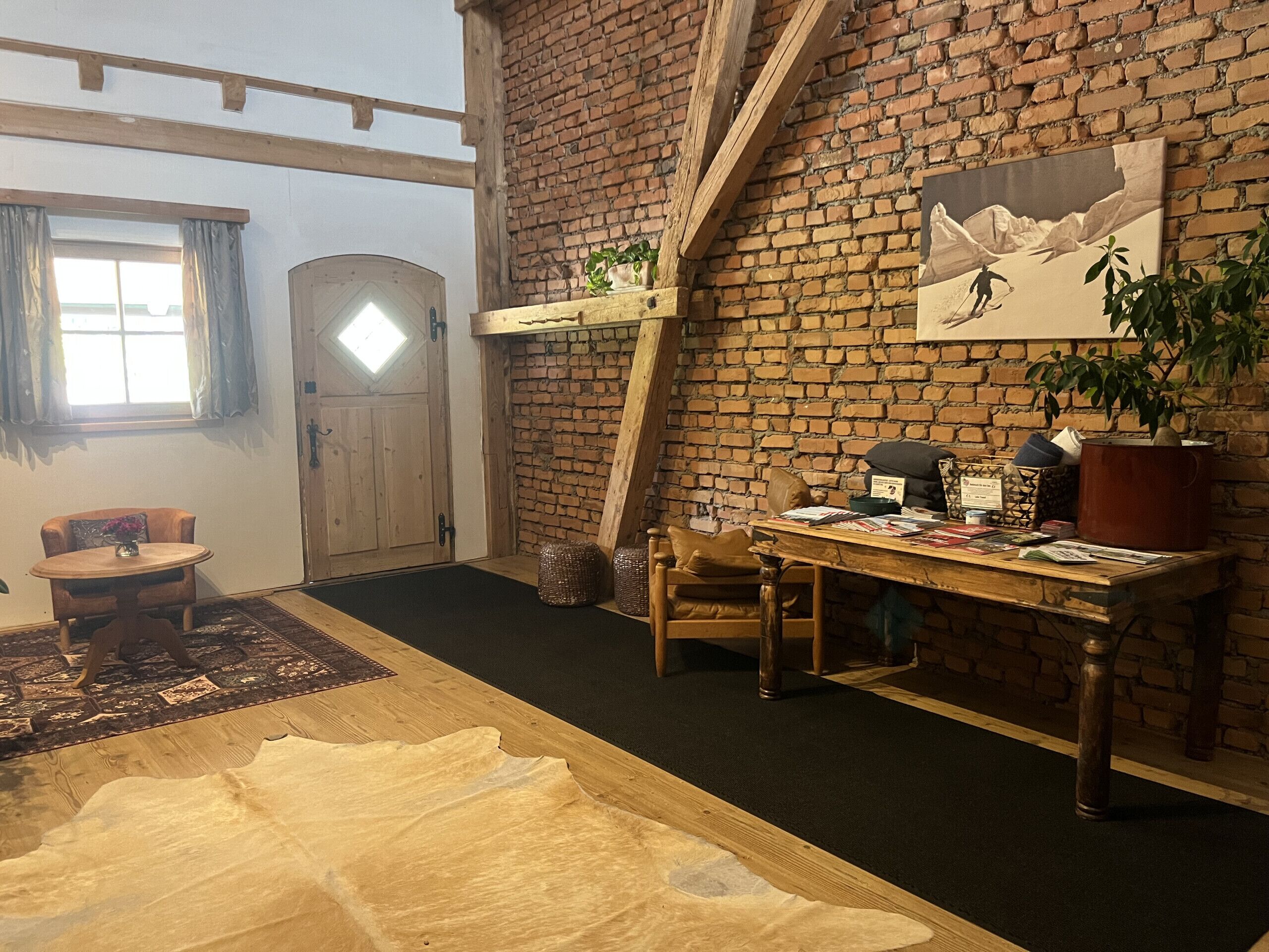 Ein Zimmer mit Backsteinwand, Holztisch, Stuhl, Teppich und einer Tür mit Fenster.